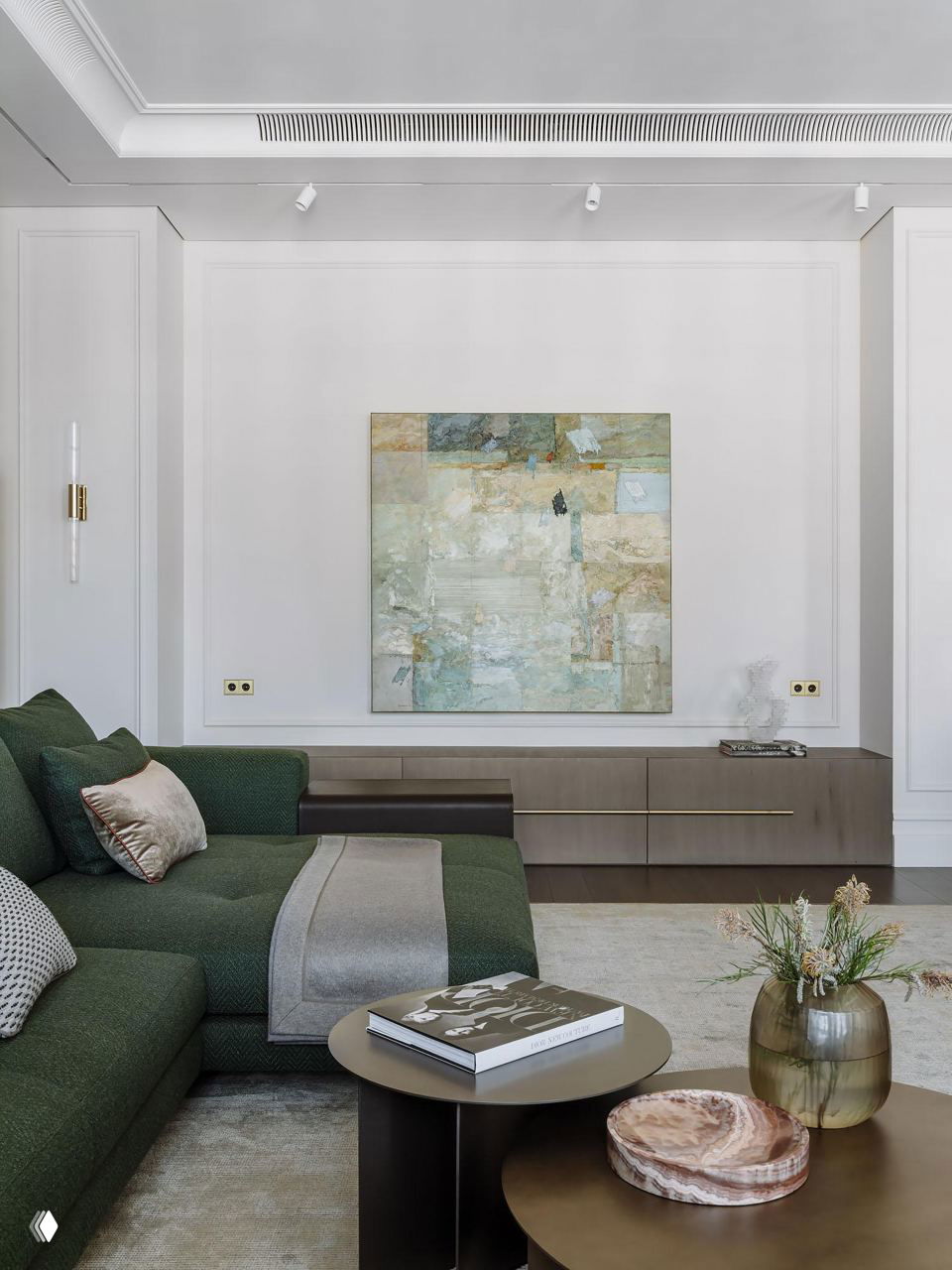 Интерьер гостиной с большим абстрактным полотном над консолью, мягким зелёным диваном, декоративными подушками и изящными латунными акцентами в отделке.