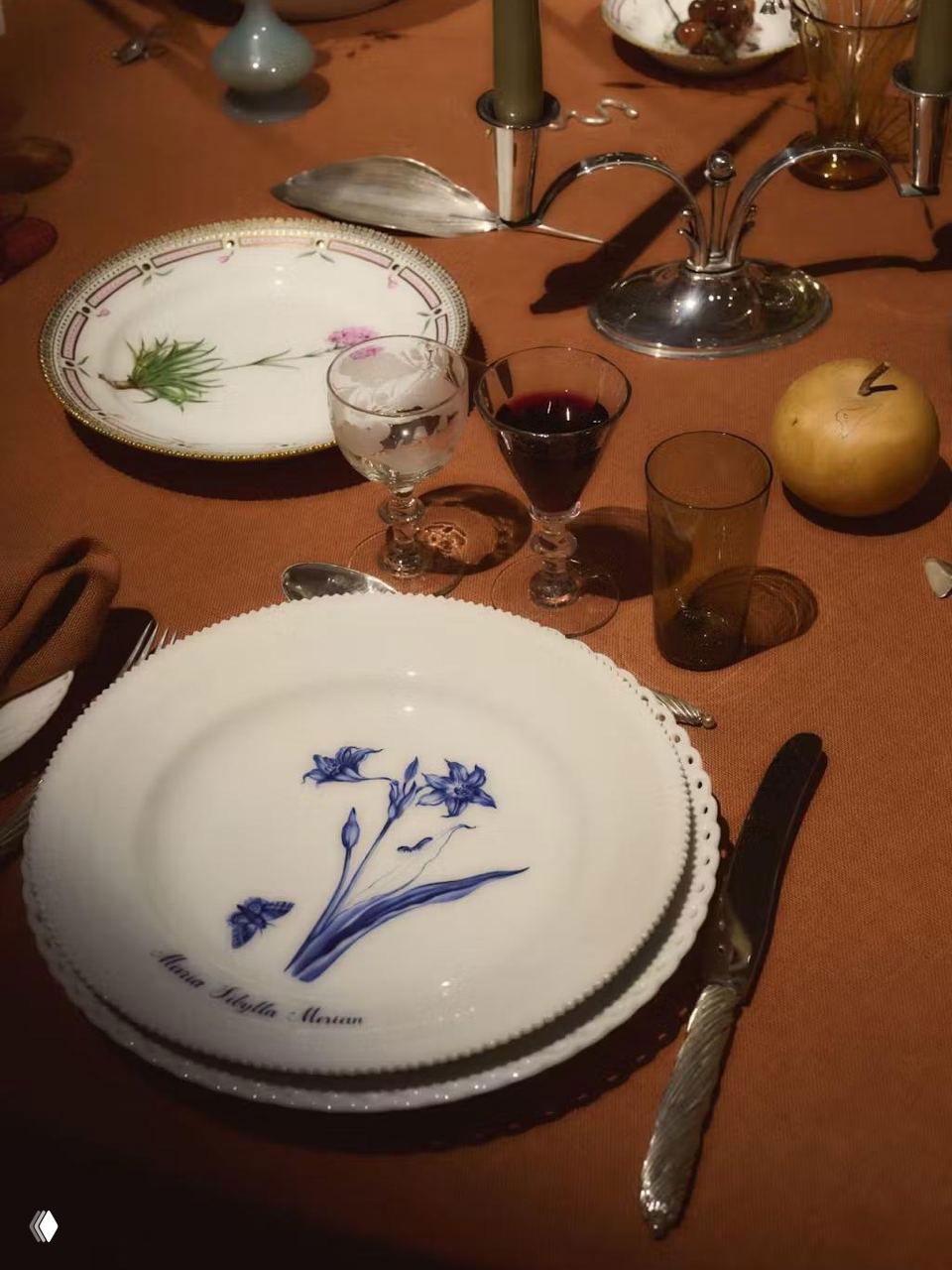 Тёплая терракотовая сервировка с фарфоровыми тарелками, бокалами и фруктом — камерная композиция с винтажными деталями и металлическими акцентами.