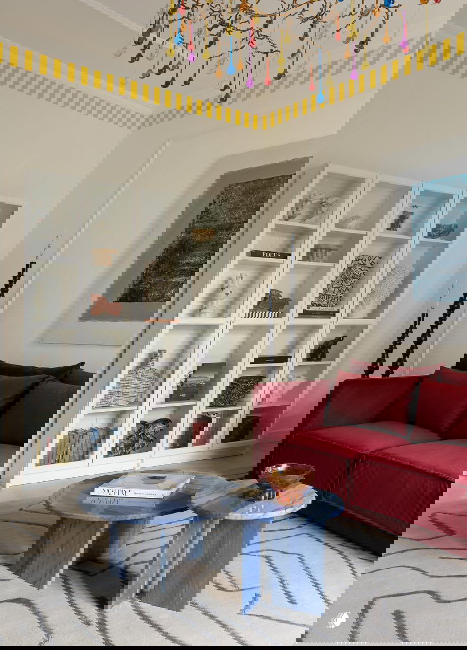 Угол гостиной с белым шкафом-витриной, красным диваном и синими мраморными кофейными столиками — декоративные детали в московской сталинке.