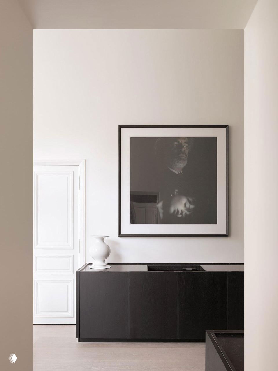 Черно-белый угол кухни или коридора: тёмный низ мебели, крупная чёрно-белая фотография в раме и светлые стены вокруг.