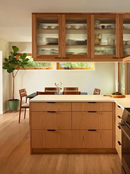 Тёплый интерьер с деревянным кухонным островом, выдвижными ящиками и подвесными шкафами со стеклом, создающий дополнительные места для хранения и визуальный объём.