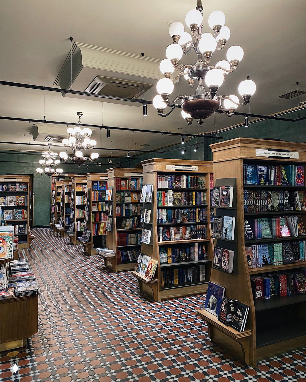 Интерьер книжного магазина с деревянными стеллажами, декоративными люстрами и узорной плиткой на полу, аккуратно расставленные книги и уютная атмосфера.