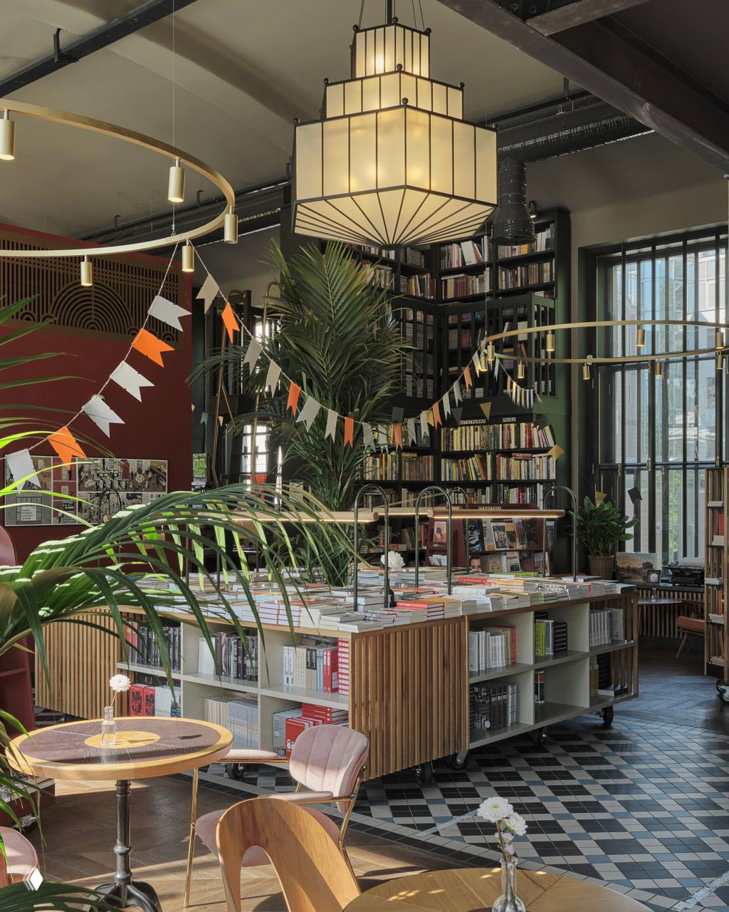 Современное книжное пространство с большими растениями, центральным выставочным столом и высокими книжными стеллажами у окон — зелёные акценты и естественный свет.