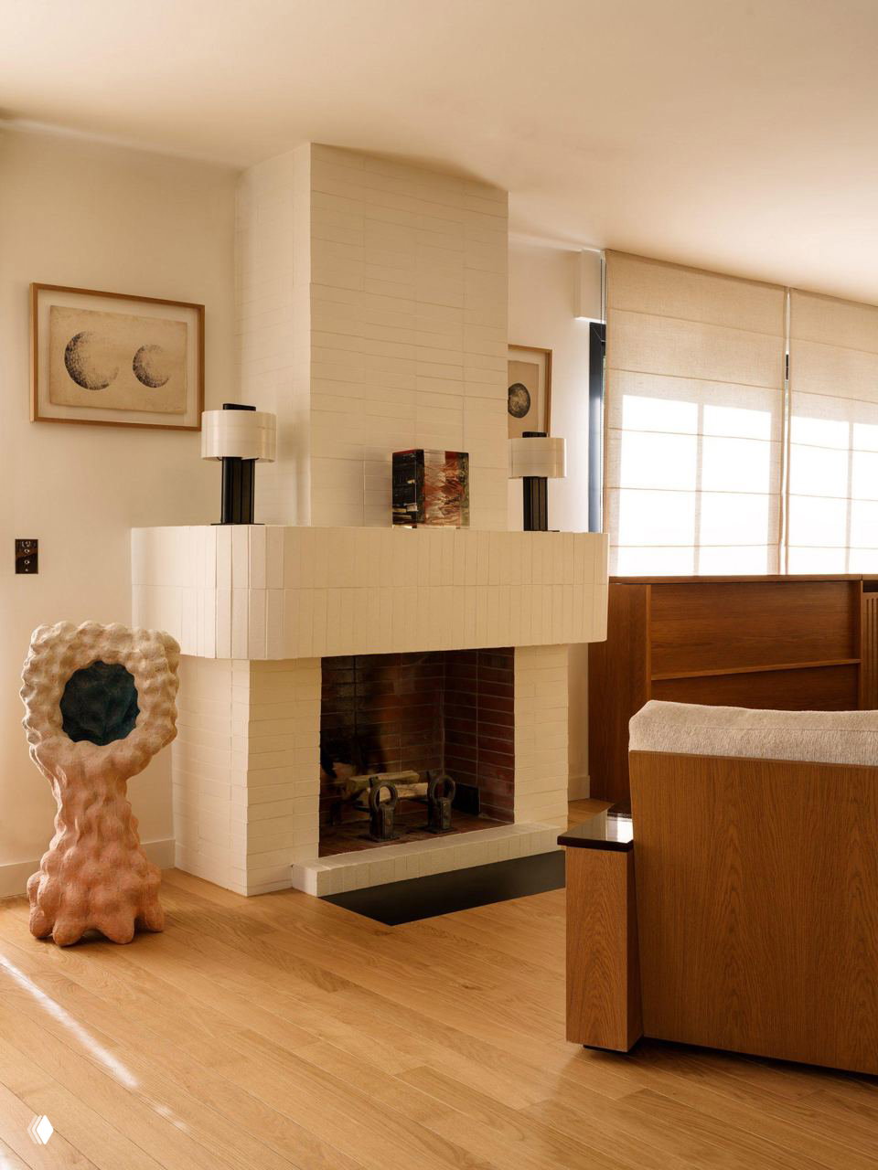 Гостиная с белым камином в кубической форме, деревянным полом и скульптурным предметом рядом — тёплая нейтральная палитра и текстуры.