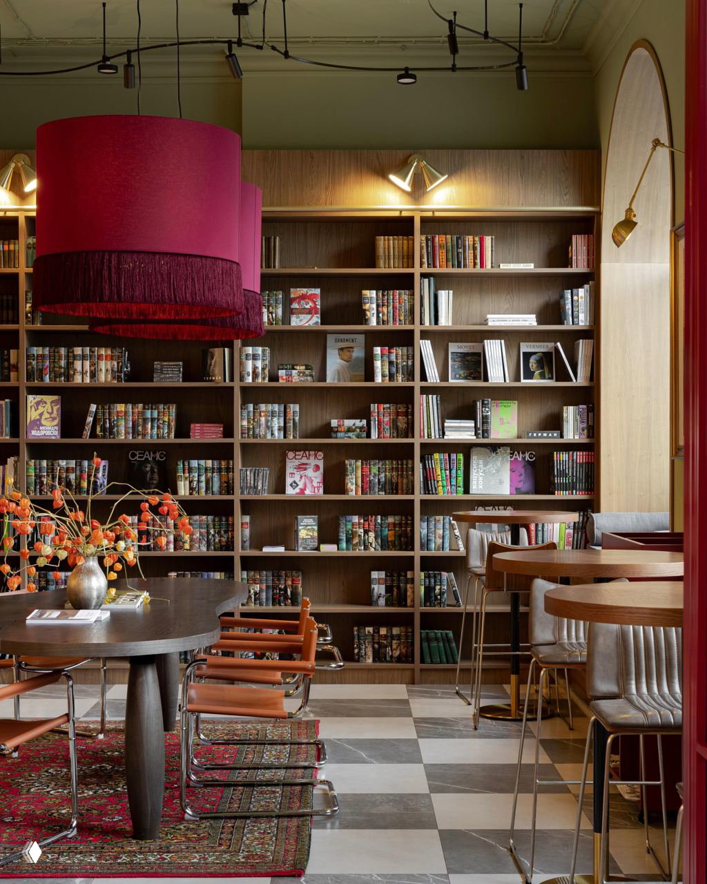 Интерьер книжного кафе с тёплыми тонами: настенные полки, столы и мягкие кресла, крупная декоративная люстра и уютное зонирование для чтения и общения.