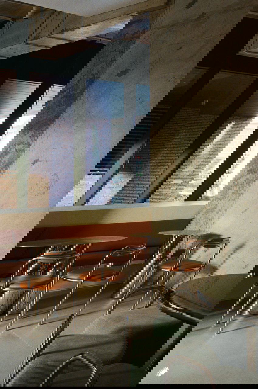 Открытый бетон с видимыми надписями на стене рядом с металлическими стульями и кожаными сидениями — контраст индустриальной фактуры и текстиля в интерьере.