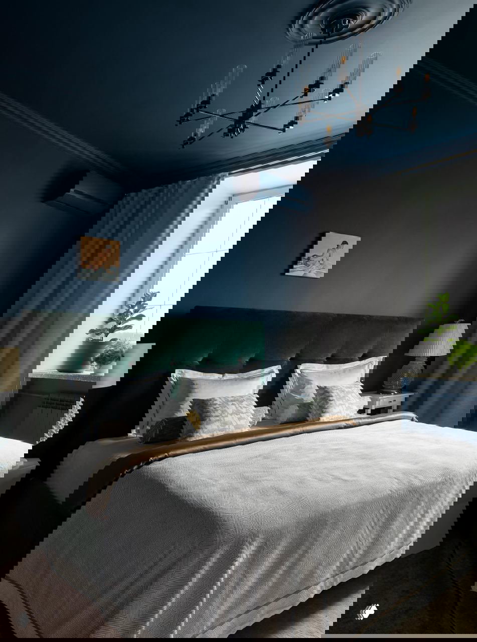 Спальня с глубоким тёмно-синим потолком и стенами, изумрудным мягким изголовьем кровати и спокойным текстилем — уютная спальня в московской сталинке.