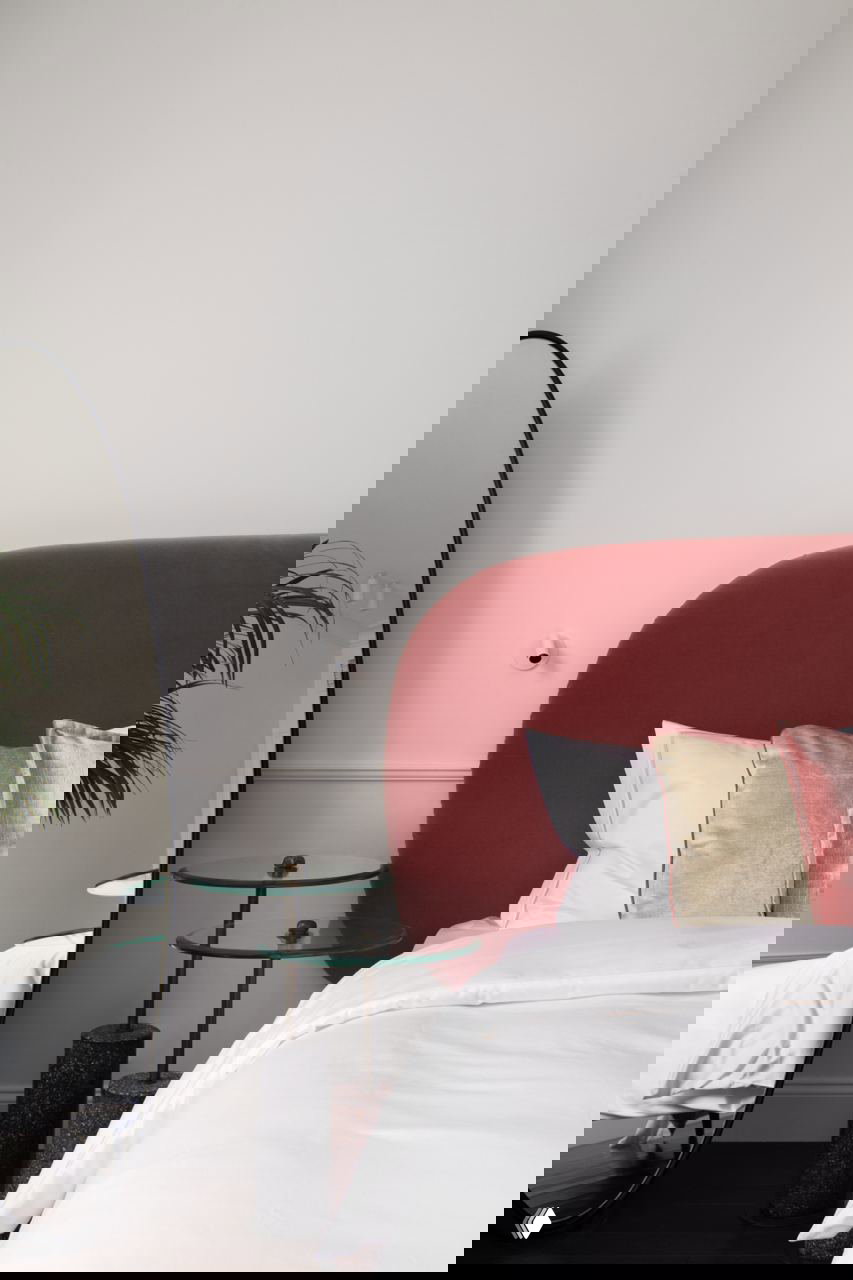 Фрагмент спальни с полукруглым бордовым изголовьем, большим напольным зеркалом и белым постельным бельем — элегантный контраст форм и текстур