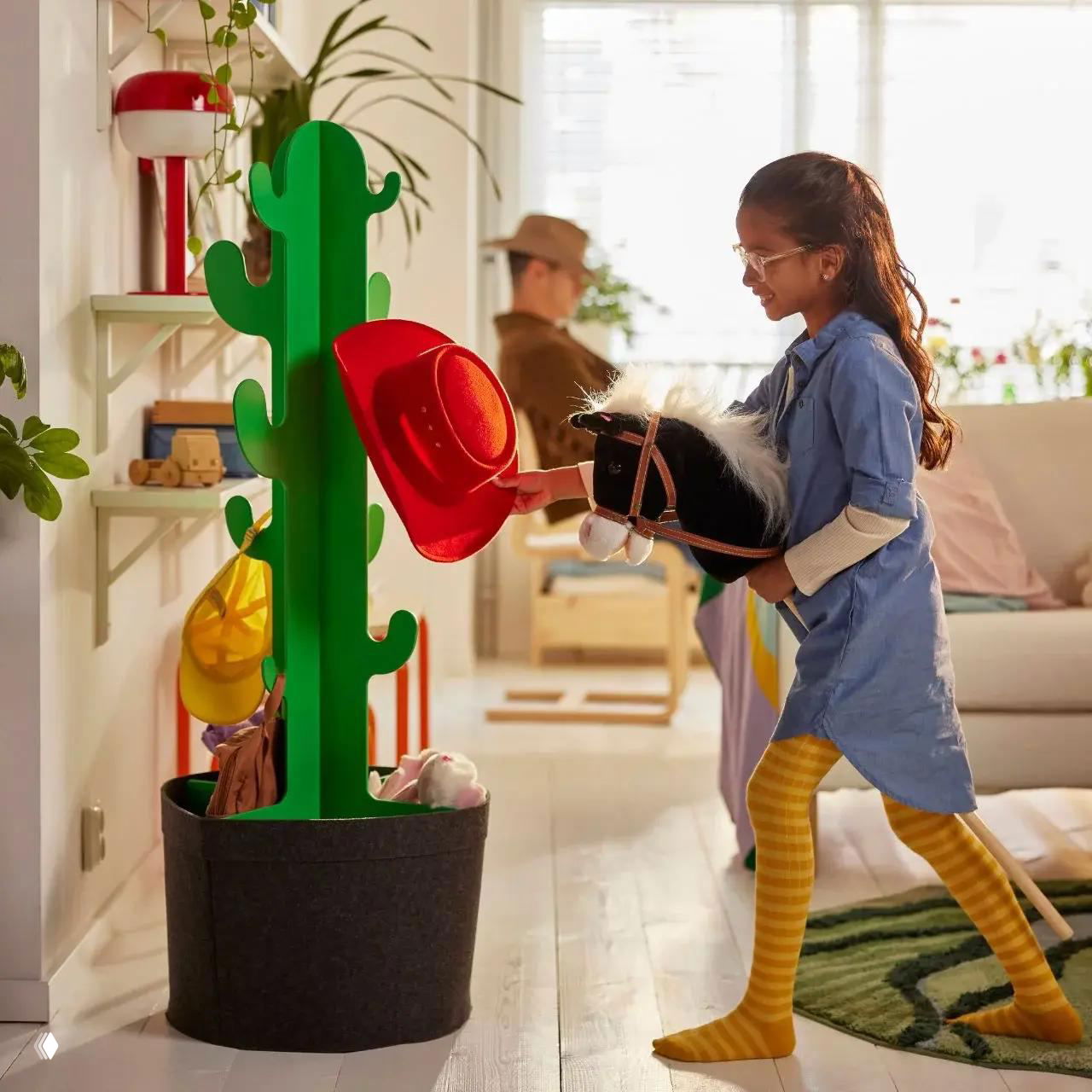Зелёная вешалка‑кактус в большой мягкой кашпо, ребёнок цепляет шляпу — пример функции и игрового дизайна из коллекции Grejsimojs.