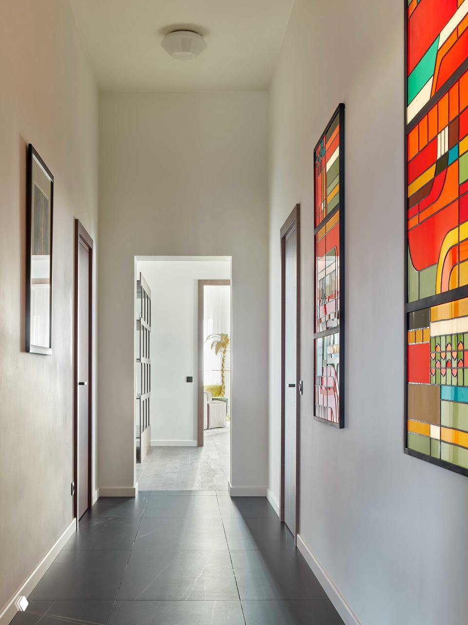 Длинный светлый коридор с белыми стенами и тёмной плиткой на полу, украшенный яркими графическими картинами вдоль стены.