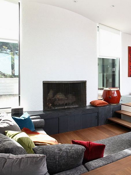 Классическая утопленная гостиная с камином, ступенчатым понижением пола и встроенными местами для сидения, мягкие текстуры и контрастные подушки.