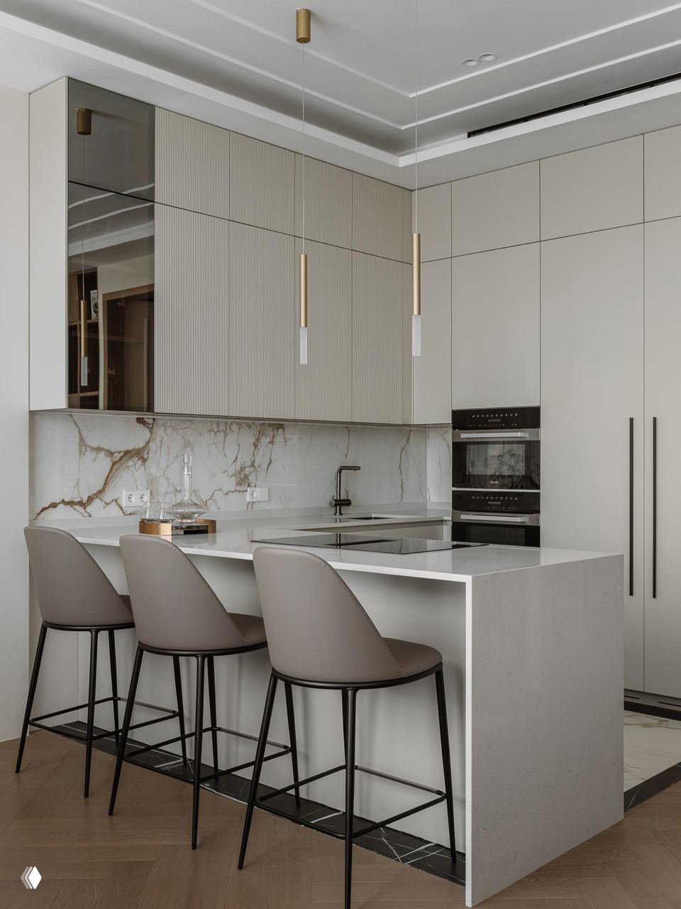 Минималистичная кухня с островом и барными стульями, светло‑бежевые фасады, мраморный фартук и тонкие подвесные светильники в золотистом тоне.