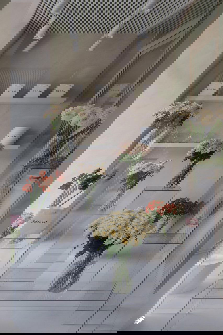 Интерьерная композиция внутри магазина: прозрачные подставки разной высоты с вазами и букетами, создающими ритм и глубину в небольшом пространстве.