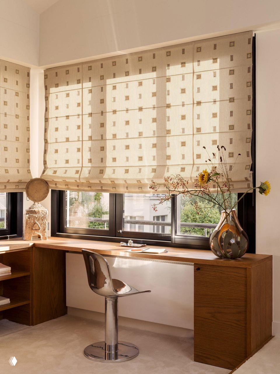 Рабочая зона у окна с деревянным столом, римскими шторами и металлическим барным стулом — спокойный уголок для письма с видом на город или сад.