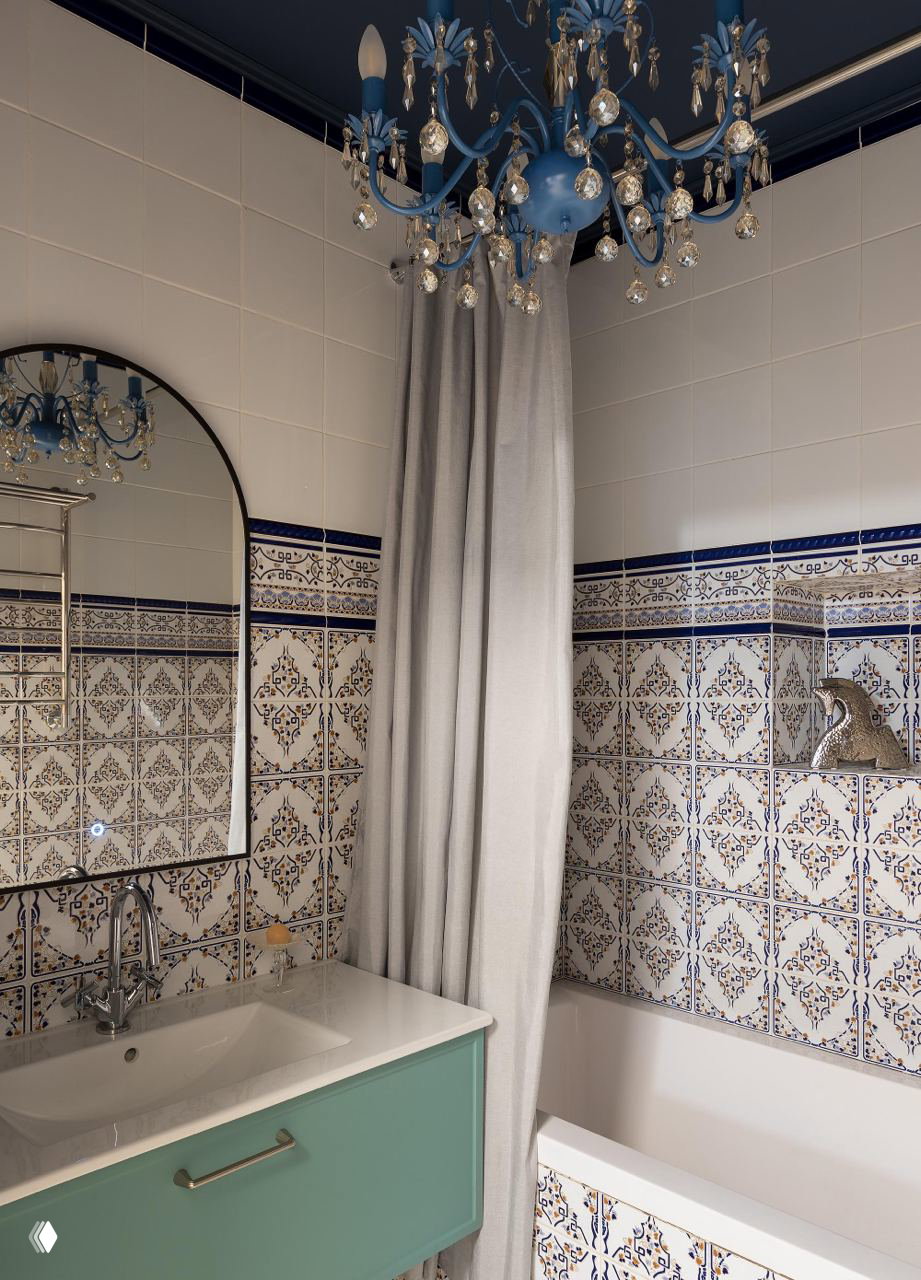Ванная комната с узорчатой сине-белой плиткой, светлой шторой и голубой люстрой — сочетание орнамента и цвета в московской сталинке.