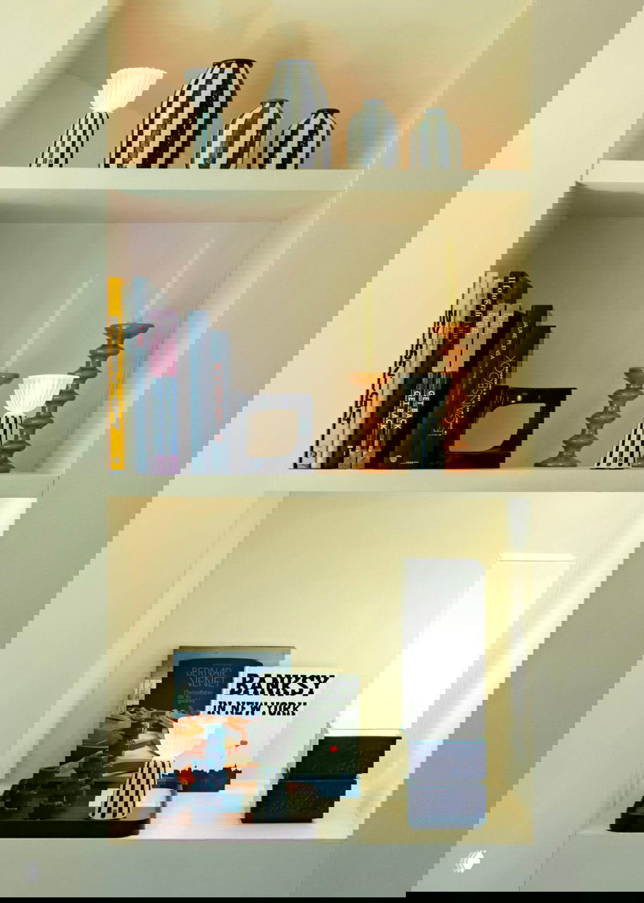 Лампы Swiing с синими полосками в нише с книгами и декоративными предметами, пример коллаборации Fermob и Maison Sarah Lavoine.