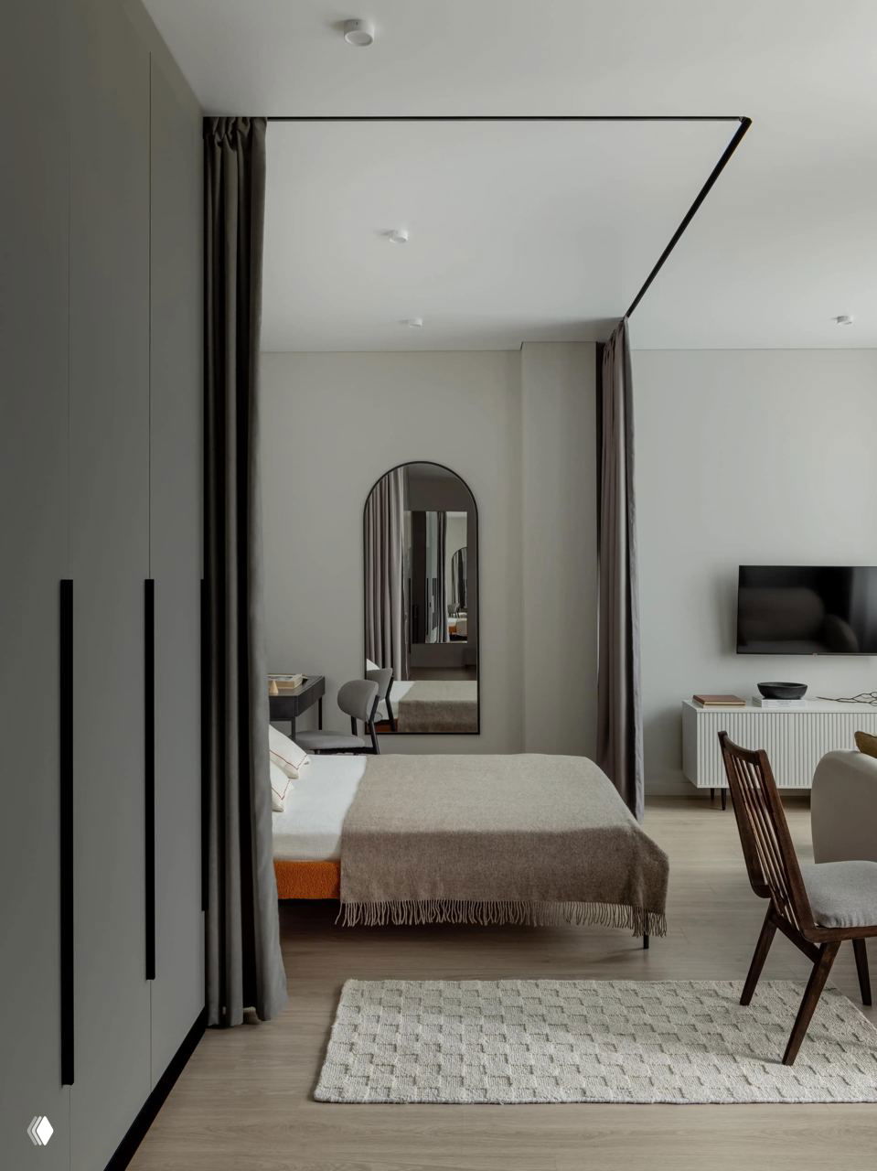 Спальная зона, объединённая с гостиной: низкая кровать у арочного зеркала, тонкие текстуры и шторы‑занавеси создают эффект многослойности и глубины в небольшом помещении.