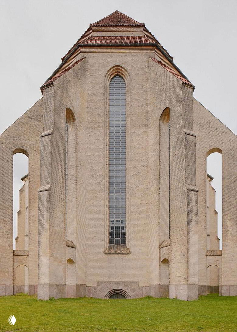 Боковой вид на кирпичную стену и высокий узкий оконный проем церкви Грундтвига, отражающий строгие пропорции и ритм арочных ниш на фасаде.