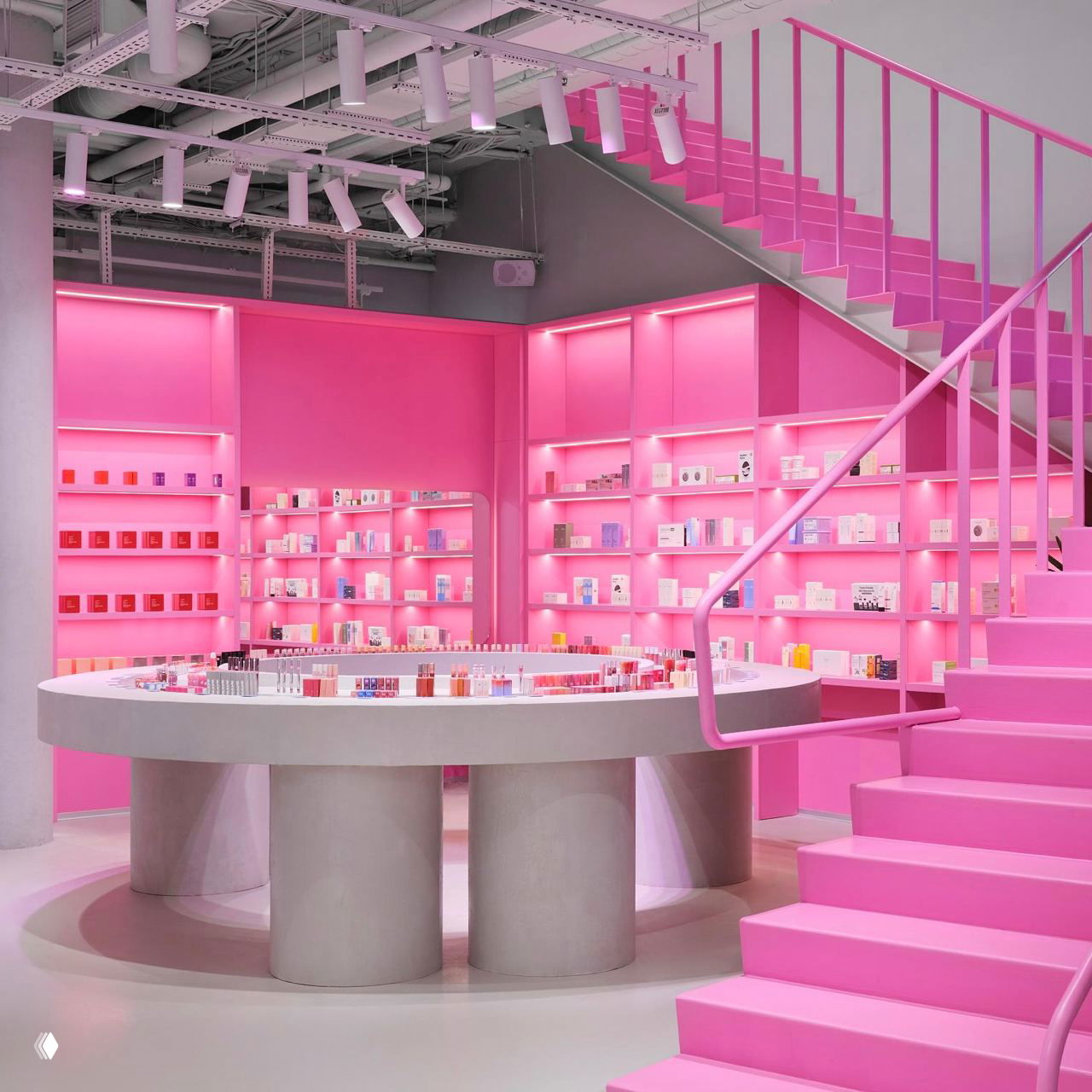 Розовая лестница и модульные полки на фоне насыщенно-розовых стен, стилизованная выкладка декоративной и уходовой косметики в минималистичной сценографии.