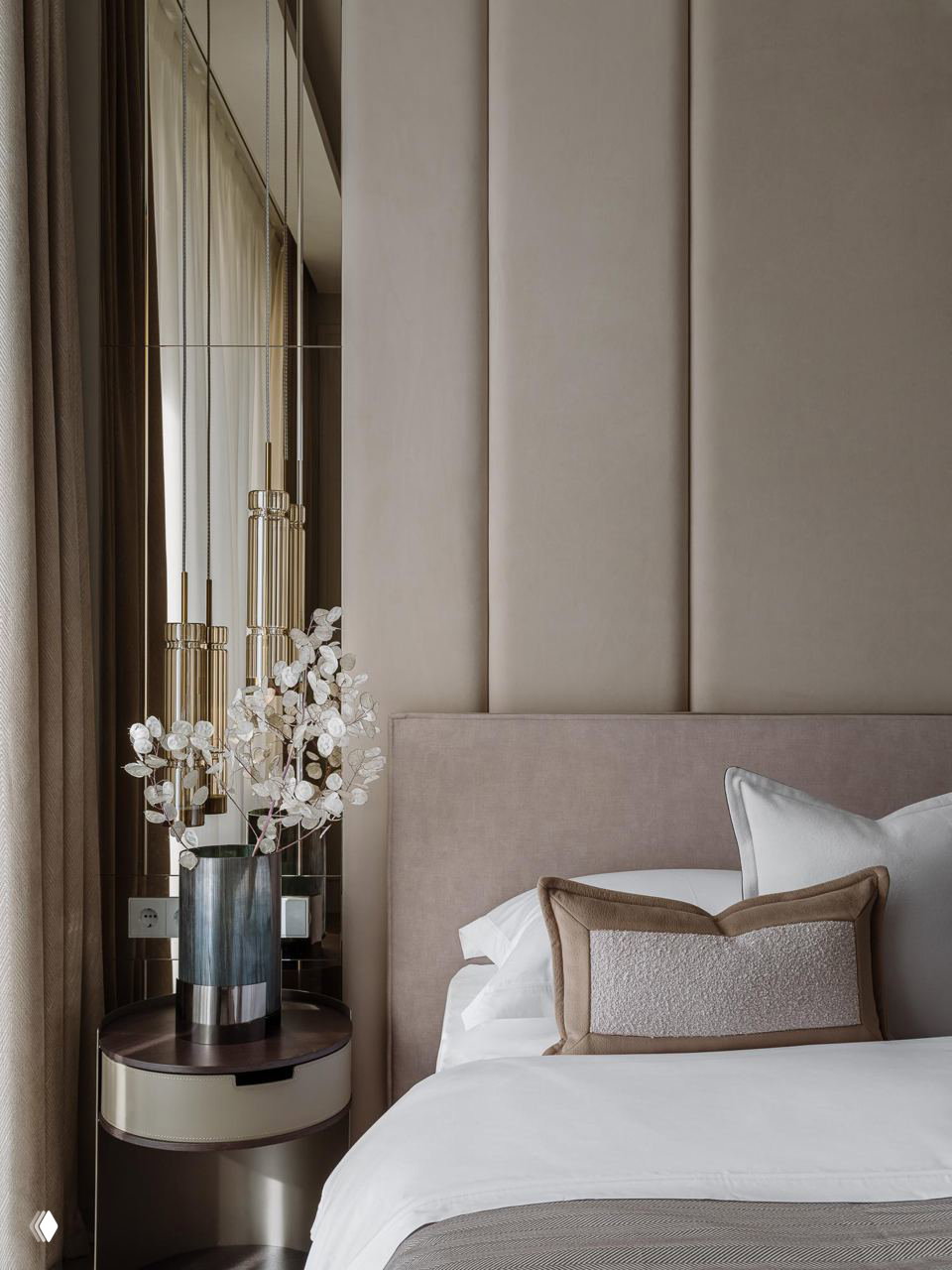 Спальня с высокой тканевой панелью за изголовьем, мягкая бежево‑пудровая палитра, декоративная ваза и зеркальные вставки у окна для эффекта глубины.