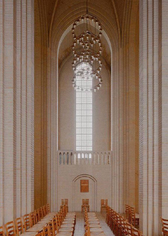 Интерьер центрального нефа церкви Грундтвига: высокие колонны, стрельчатые своды и длинное окно, через которое мягко падает дневной свет.