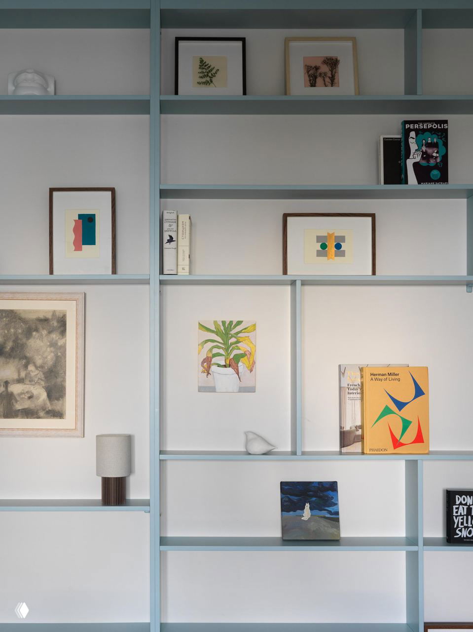 Открытые стеллажи пастельно‑голубого оттенка с книгами, рамками и маленькими декоративными объектами — пример упорядоченного хранения в малой площади.