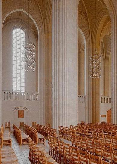Ряды деревянных стульев в нефе церкви Грундтвига, стрингентная ритмика колонн и хрустальные люстры, создающие спокойную атмосферу внутри.