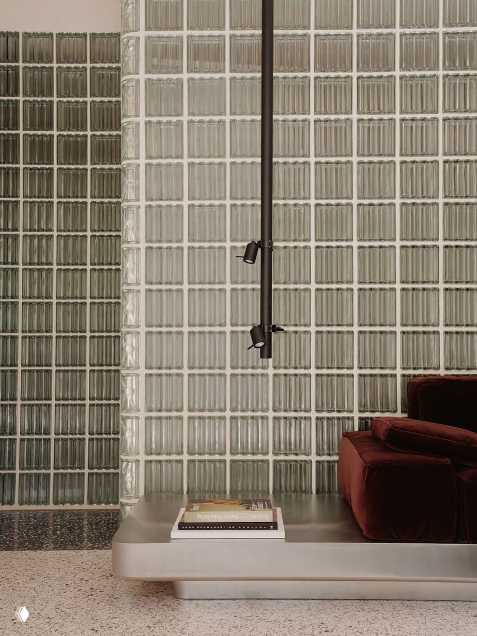 Крупный план изогнутой поверхности из стеклоблоков с подвесными направленными светильниками и фрагментом бордового дивана на переднем плане — игра света и текстур.