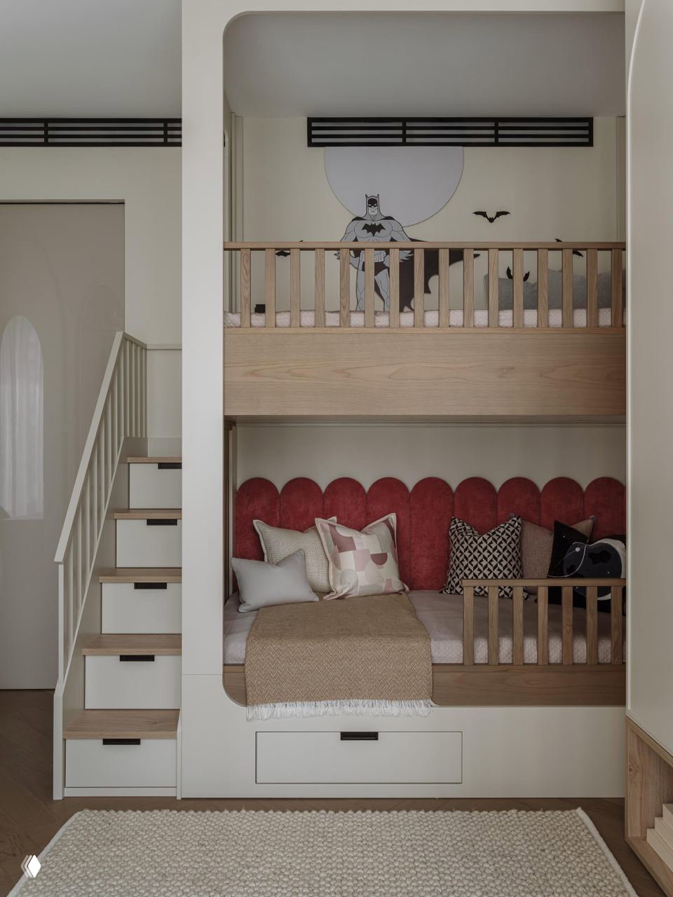 Детская зона с двухъярусной кроватью в светлой древесной отделке, мягкими текстильными элементами и рисунком Бэтмена на стене — игривый, но сдержанный дизайн.