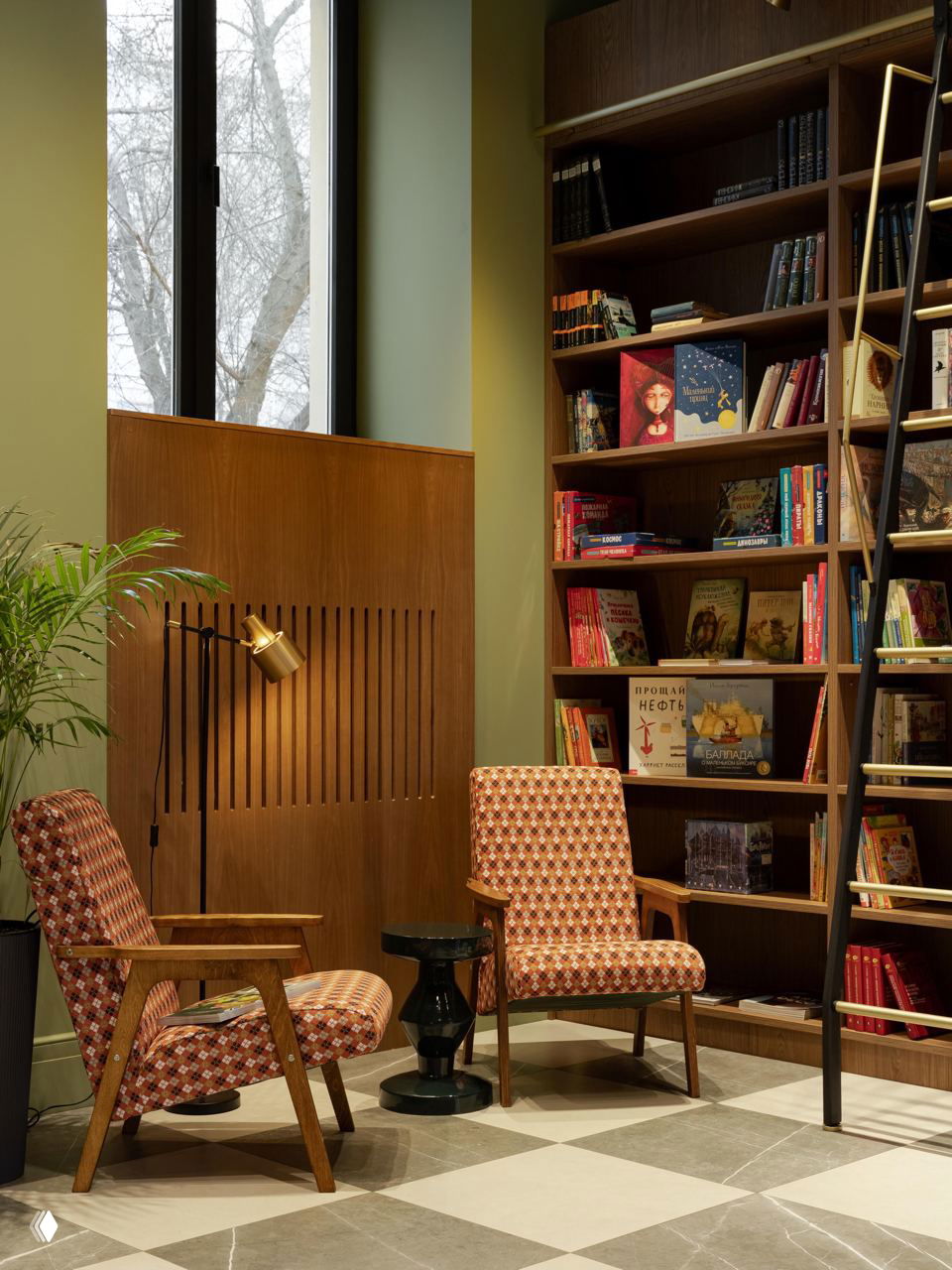 Уютный читальный угол с двумя креслами в ретро-обивке на фоне высоких деревянных стеллажей с книгами и большой виниловой плиткой на полу — атмосфера камерной библиотеки.