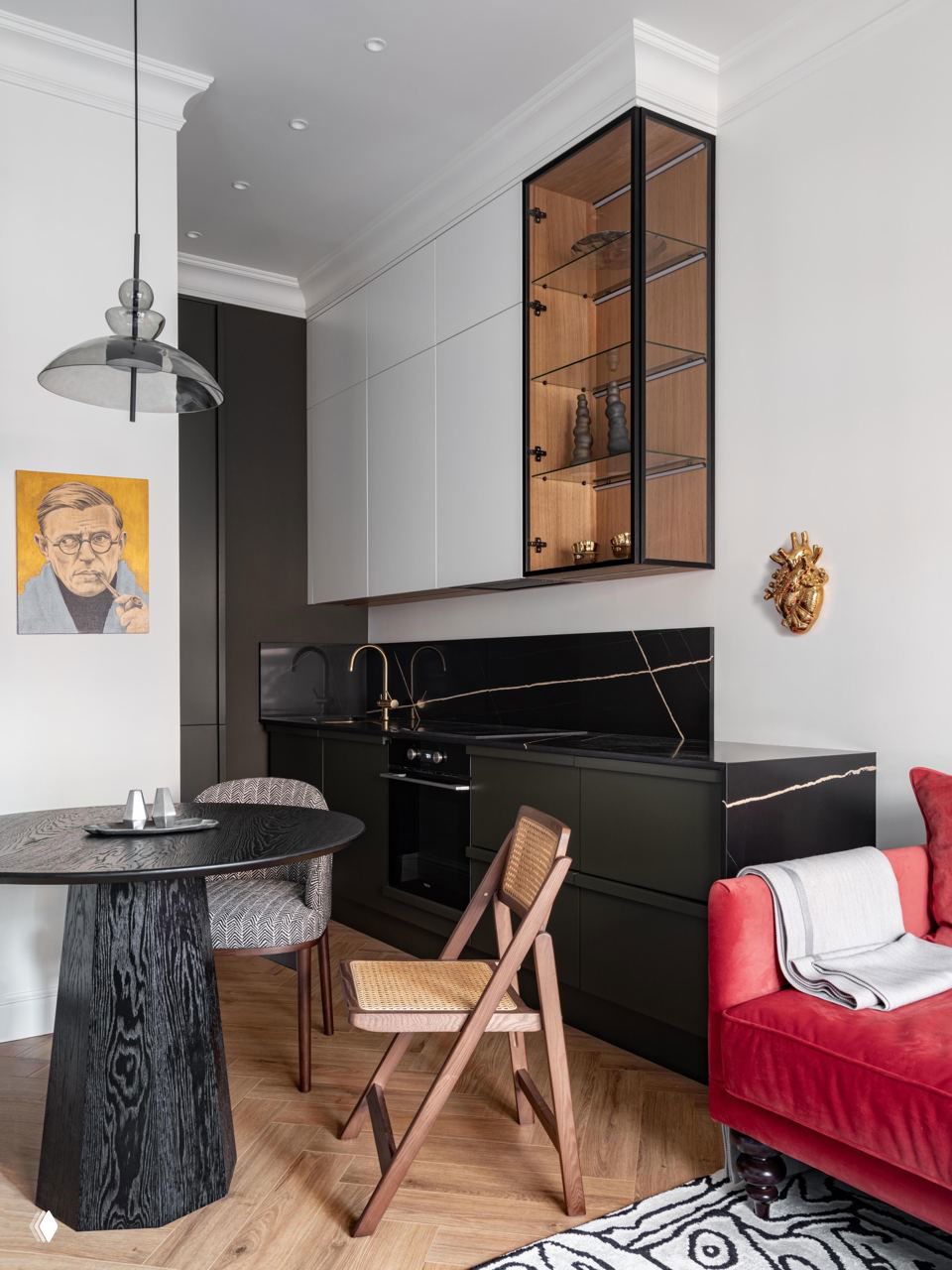 Кухонный угол в той же квартире: чёрный кухонный гарнитур с золотыми акцентами, обеденный стол и кресло на фон паркетного пола и текстиля.