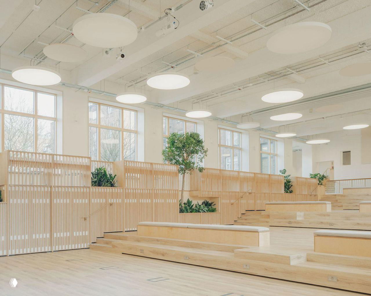 Общий вид учебного центра: минималистичные скамьи, встроенные клумбы и крупные круглые потолочные светильники, равномерно освещающие пространство.