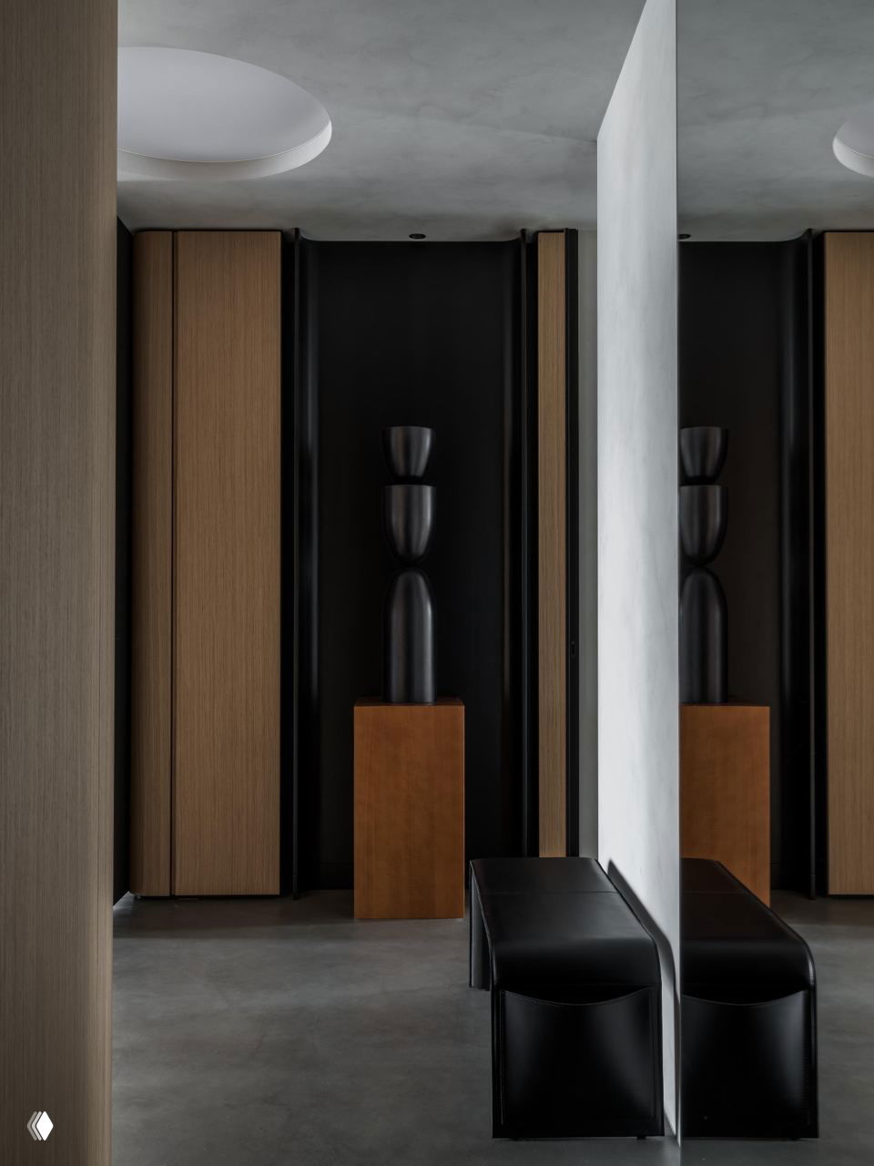 Интерьеры прихожей с зеркалами и тёмными скульптурами на постаментах, контраст дерева и чёрных декоративных элементов в минималистичном пространстве.