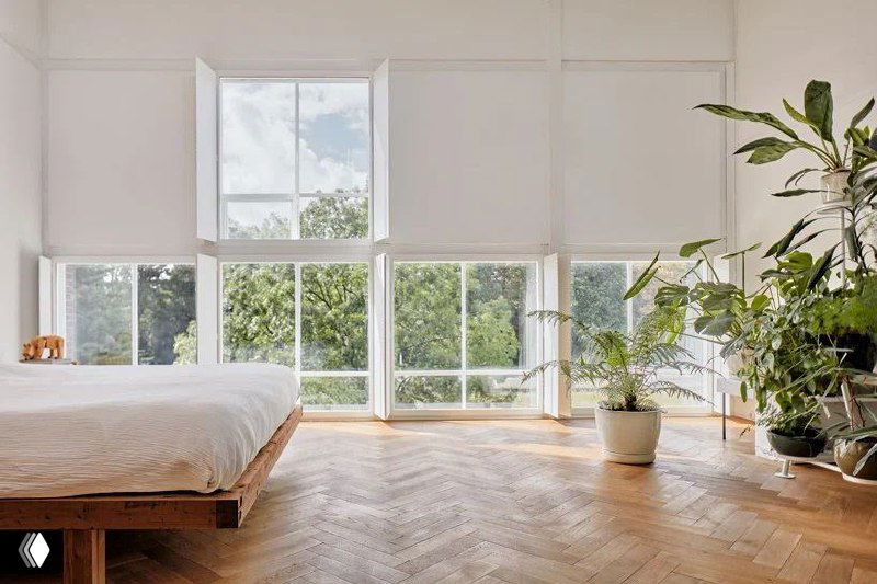 Светлая спальня с большими окнами и паркетным полом, окружённая растениями — пример интерьера, требующего правильного ухода за деревом.