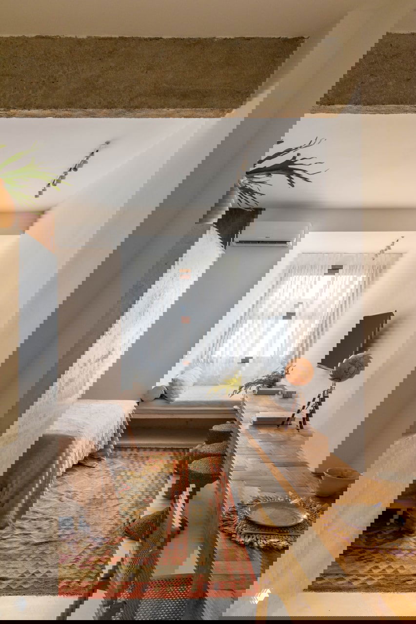 Общий вид студии: бетонные перекрытия, белые стены, длинная деревянная столешница у окна и ниша с местом для отдыха у светлого окна.