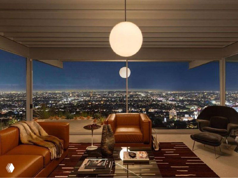 Дневной интерьер дома Шталя: гостиная и обеденная зона рядом с террасой, стальной каркас и открывающиеся виды на Лос‑Анджелес через большие стеклянные стены.