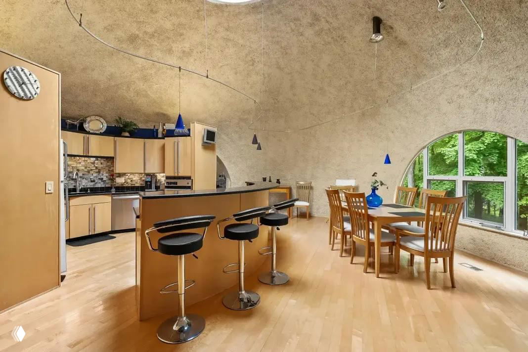 Кухня-столовая под куполом: барная стойка с высокими стульями, обеденный стол и большие арочные окна, наполняющие помещение светом.