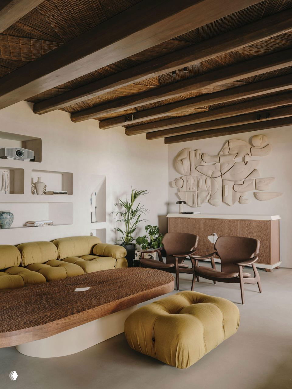 Гостиная с низким мягким диваном горчичного цвета, плетеным столом и скульптурными нишами на стене — теплая минималистская палитра и текстуры.