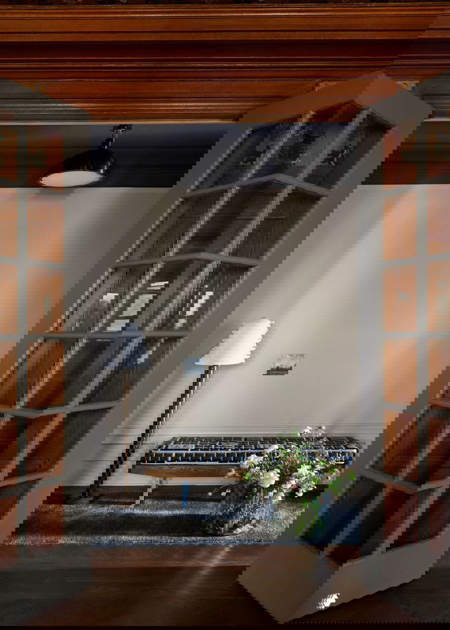 Проход между комнатами с серыми дверьми и минималистичной скамьёй; композиция светлых стен и деревянных рам дверей.