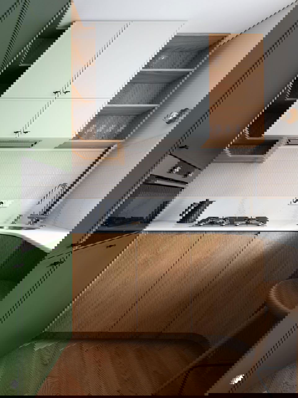 Компактная кухня с зелёными шкафами, деревянными фасадами внизу, белой столешницей и встроенной газовой варочной панелью