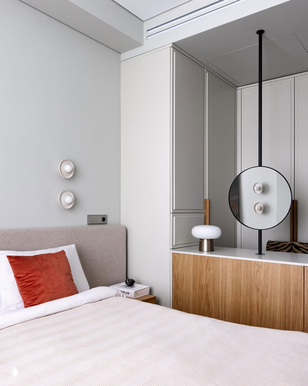 Спальня в спокойных бежевых тонах: изголовье кровати, коралловая декоративная подушка, встроенные шкафы и минималистичное освещение