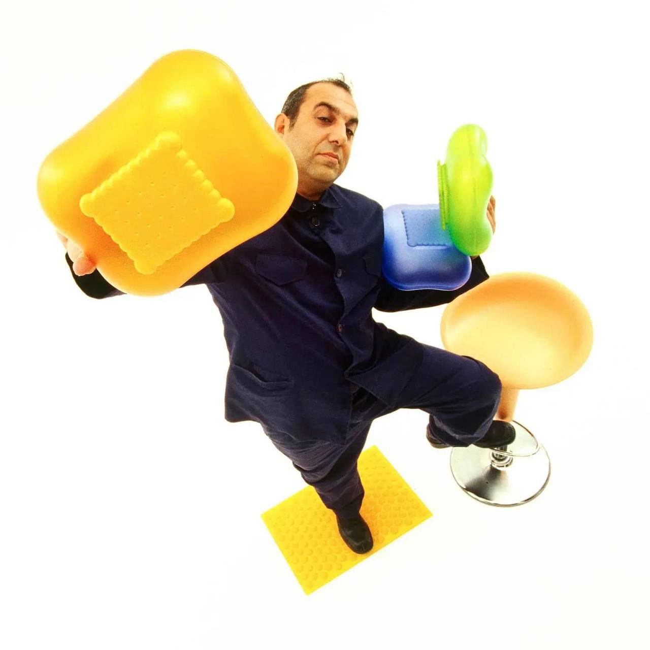 Фотография дизайнера на белом фоне с яркими пластиковыми стульями и табуретом — экспрессивная демонстрация цветных предметов мебели