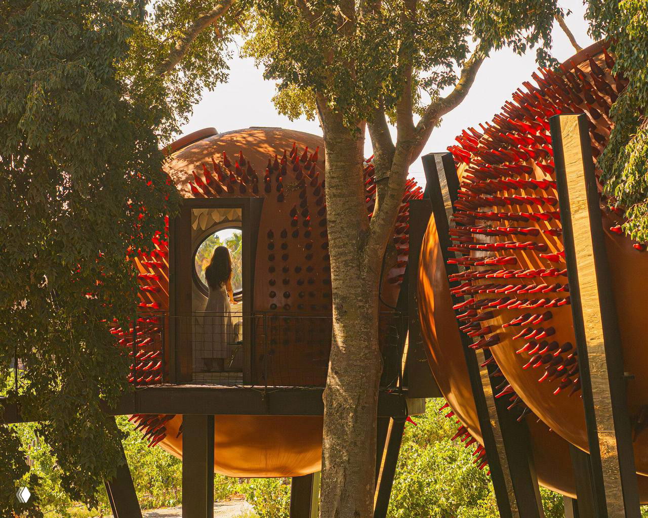 Крупный план трёх медных сфер с фактурой и вкраплениями стекла; видна входная арка и человек на балконе, подчёркивающий масштаб.