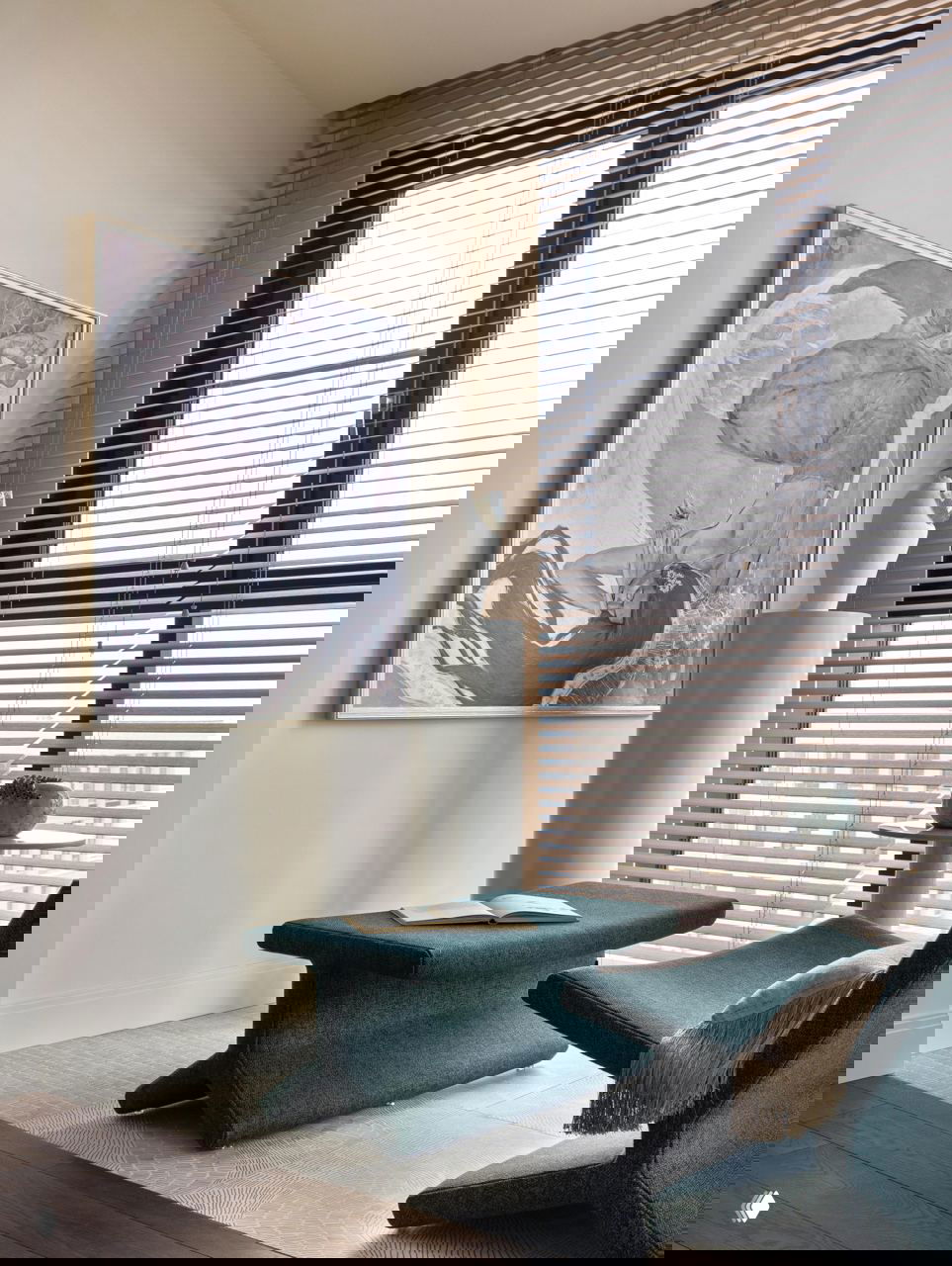 Уютная зона у окна с зелёными креслом и банкеткой, большое художественное полотно на стене и жалюзи, создающие спокойную атмосферу.