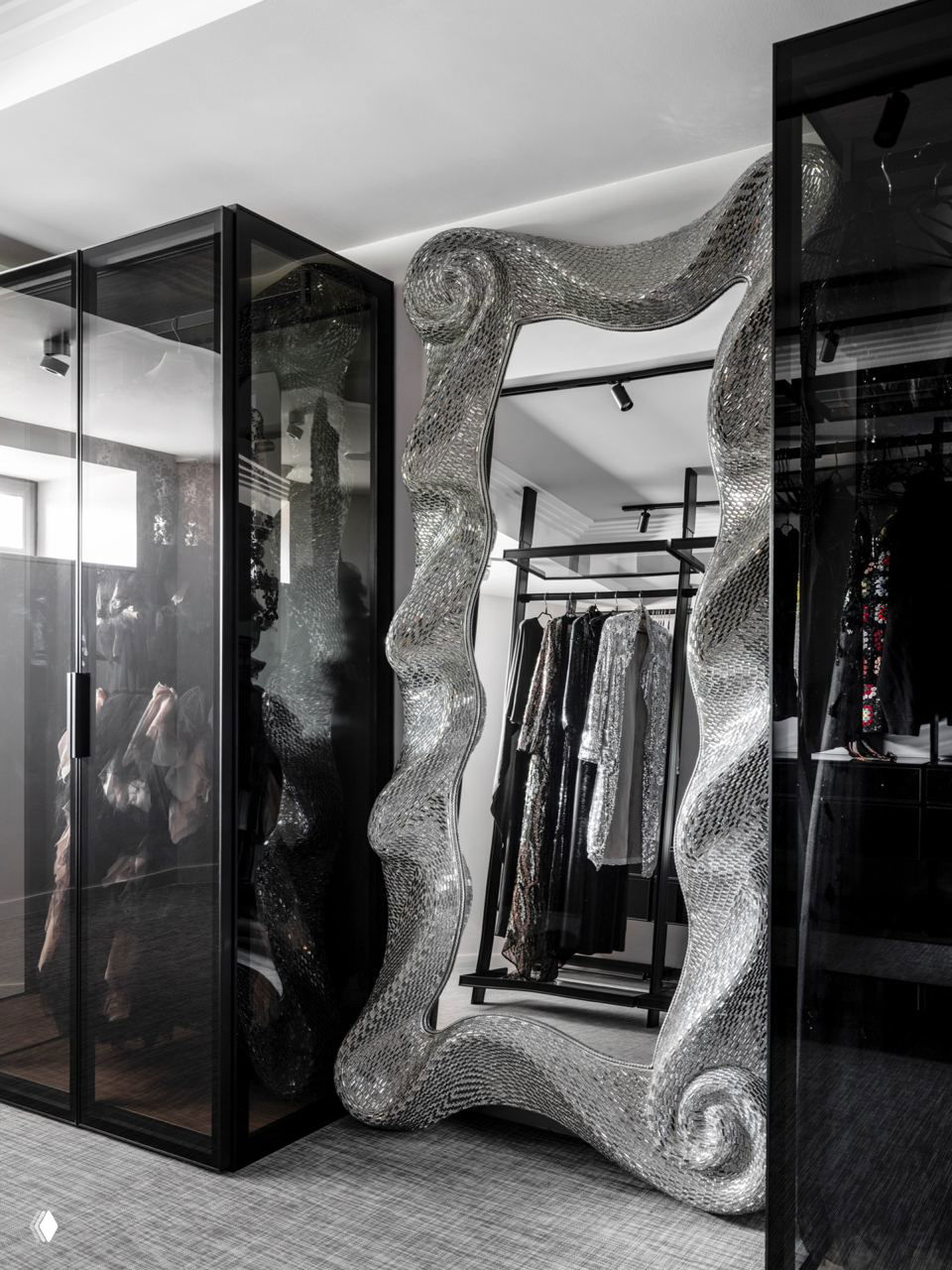 Пространство гардеробной с большим декоративным волнистым зеркалом в серебристом оформлении и тёмными шкафами — металлические акценты в интерьере.