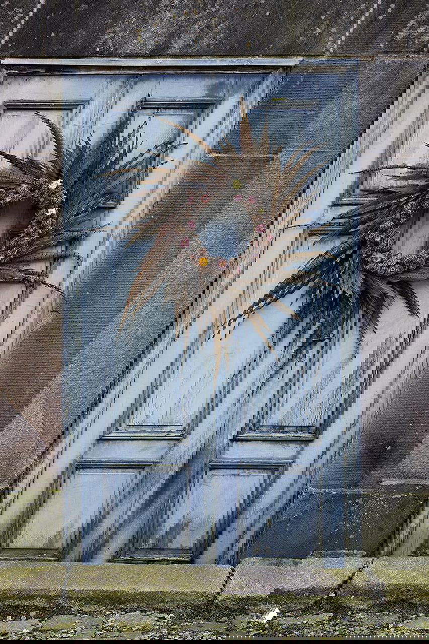 Старая голубая деревянная дверь датского поместья на Фюне украшена венком из сухих веток, шишек и засушенных полевых цветов на Рождество в поместье на Фюне.