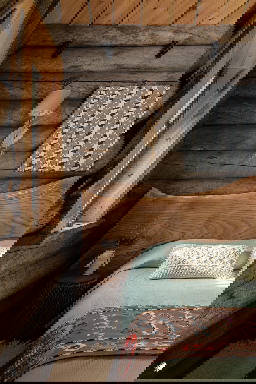 Спальня в банном доме: натуральная деревянная изголовье из цельного массива, текстиль в природных тонах и стены из бревен кело.