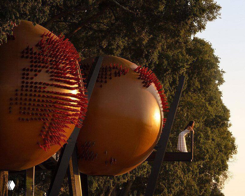 Съёмка снизу показывает ряд сфер Atomos под кронами деревьев; на поверхности видна текстура переработанных материалов и деталей.