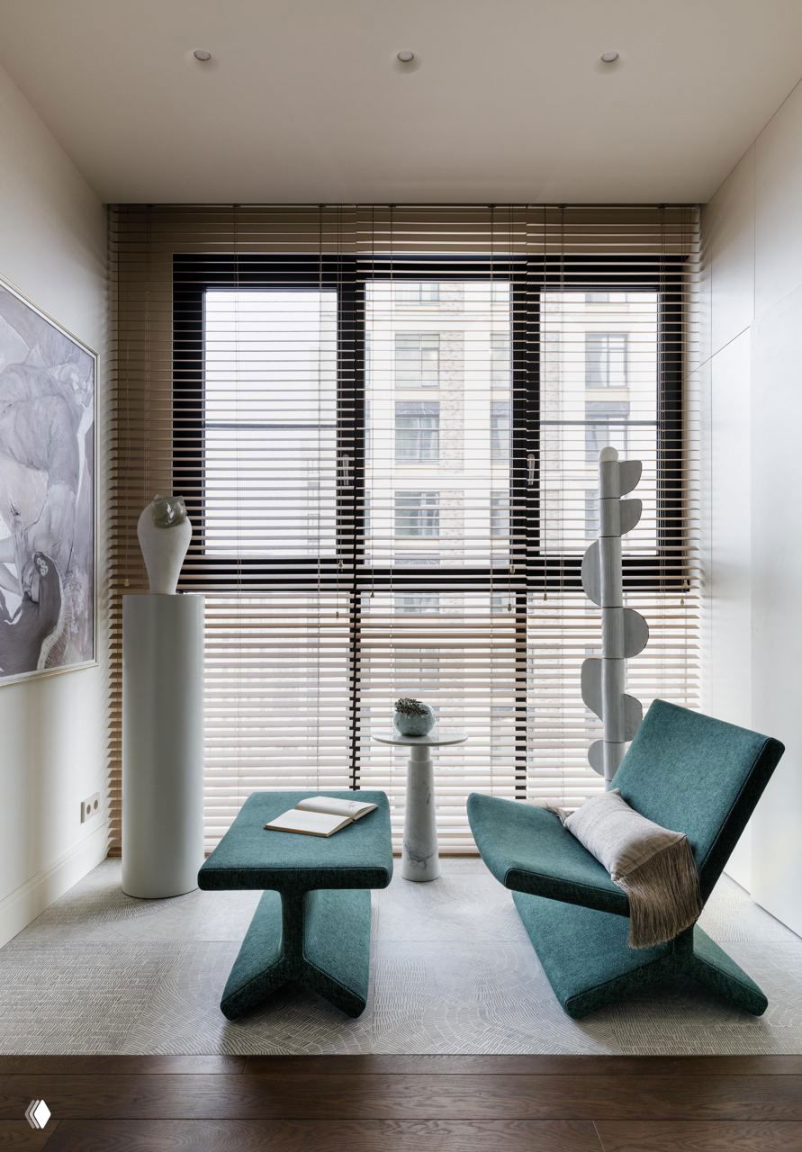 Маленький уголок у панорамного окна: банкетка и кресло, скульптурные декоративные колонны и текстильный ковёр в нейтральных тонах.