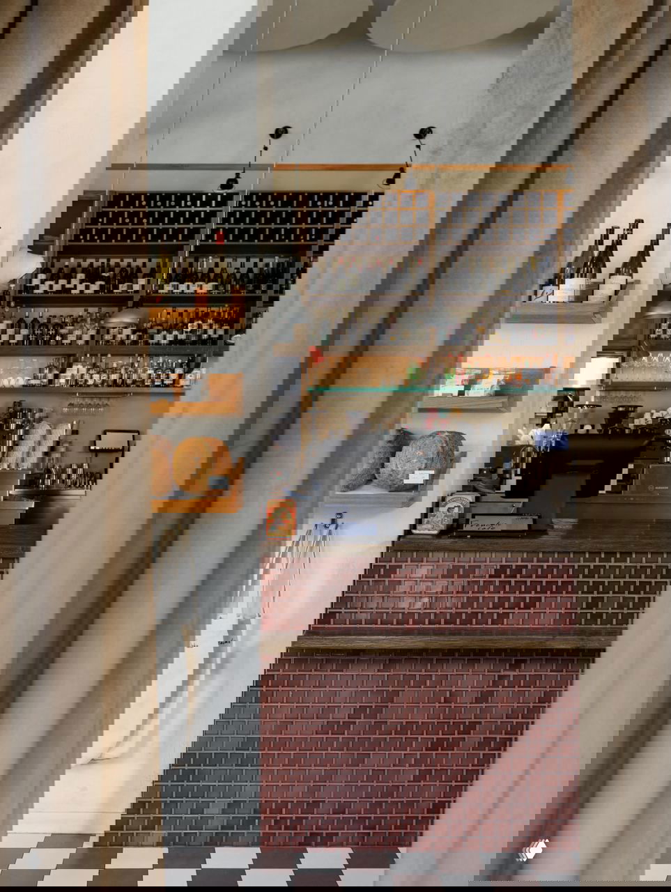 Вид сквозь шторы на барную стойку с керамической плиткой, полки с бутылками и полками с хлебом; композиция создаёт ощущение кафе-пекарни.